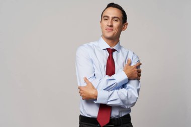 Beyaz gömlekli, kırmızı kravatlı bir adam elleri açık bir arka planda kendine sarılıyor.