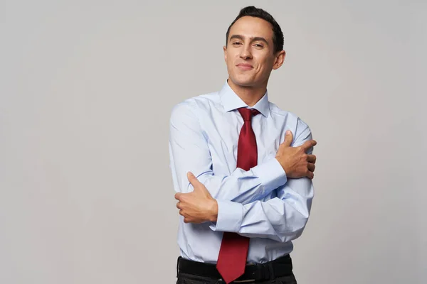 En mann med rødt slips i hvit skjorte klemmer seg selv med hendene på en lys bakgrunn – stockfoto
