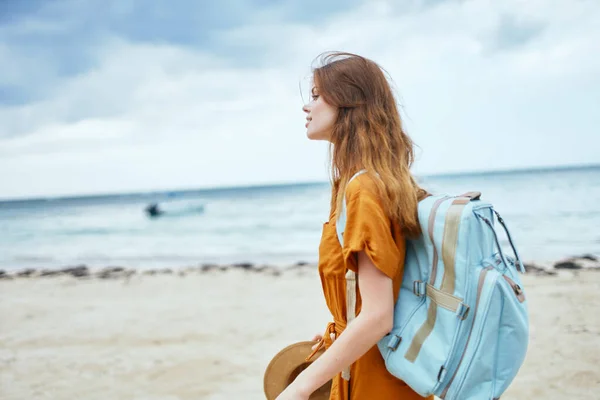 Frau in Sonnenbekleidung mit Rucksack auf dem Rücken spaziert am Strand in der Nähe des Meeres — Stockfoto