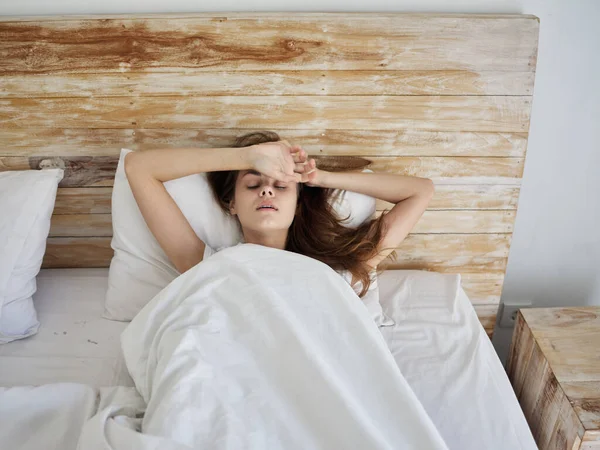 Жінка лежить в ліжку під кришками руки на лобі — стокове фото