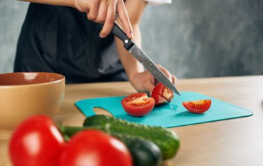 Mutfakta siyah önlüklü bir kadın sebze doğruyor salata diyeti yapıyor.