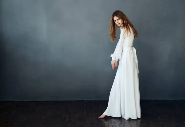 Mujer en vestido blanco posando sobre un fondo oscuro descalzo en pleno crecimiento — Foto de Stock