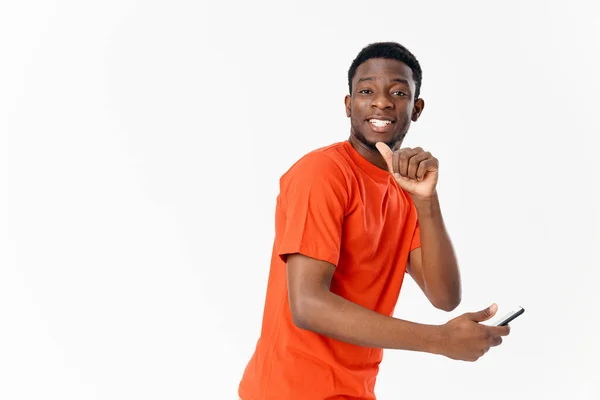 Jovem afro-americano sorrindo e segurando um telefone touchscreen em sua mão em um fundo leve — Fotografia de Stock