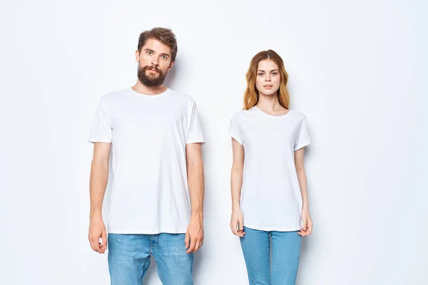 Весела молода пара в білих футболках і джинсах студії позує на світлому фоні — стокове фото