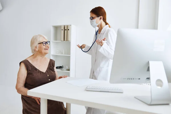 Donna anziana che indossa una maschera medica su esame da uno stetoscopio infermiera — Foto Stock