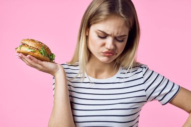 Elinde fast food olan neşeli bir kadın lezzetli pembe arka planda atıştırıyor.