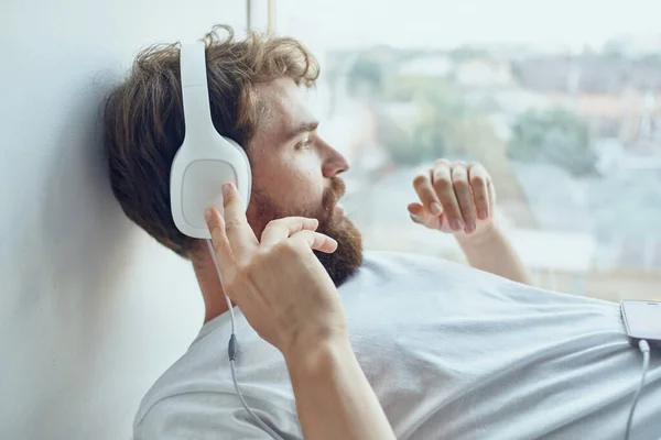 Άνδρας με λευκό t-shirt ξαπλωμένος στο περβάζι φορώντας ακουστικά διασκέδαση — Φωτογραφία Αρχείου