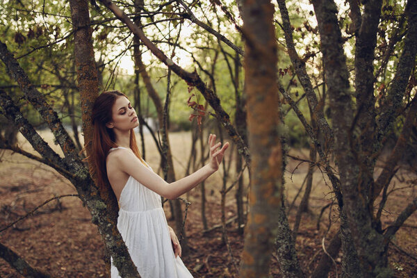 Woman in white dress leaning on a tree in forest
