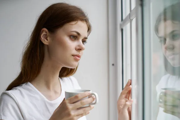 Vrouw bij het raam met een kopje in de hand Reflectie op glazen kamer interieur — Stockfoto