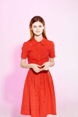 Kırmızı elbiseli güzel kadın çekici poz veriyor. Pembe arka plan.