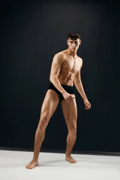 Uomo in pantaloncini neri con un corpo muscoloso su sfondo scuro — Foto Stock