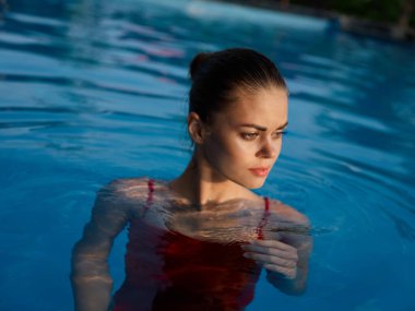 Kırmızı mayo giymiş güzel bir kadın havuz havuzunda lüks bir tatil yapıyor.