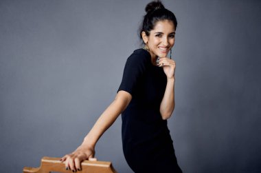 Sandalyenin yanında siyah elbiseli güzel bir kadın. Lüks moda, karanlık arka plan.