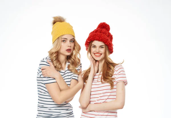 Δύο φίλες με πολύχρωμα καπέλα στέκονται η μία δίπλα στην άλλη ποζάροντας ελαφρύ φόντο — Φωτογραφία Αρχείου