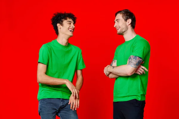 Due amici allegri in t-shirt verdi che comunicano emozioni sfondo rosso — Foto Stock