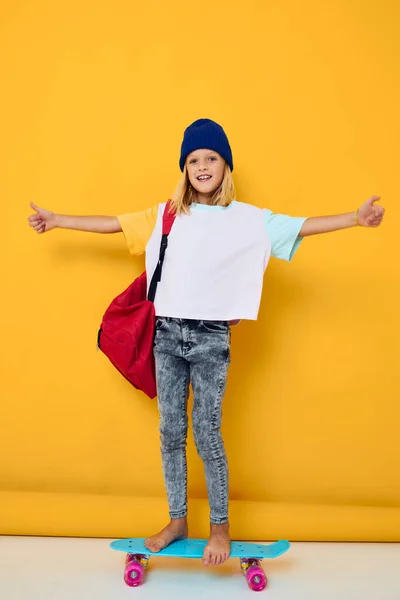 Stylisches Mädchen fährt Skateboard mit rotem Rucksack auf gelbem Hintergrund — Stockfoto