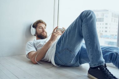 Pencerenin kenarına uzanmış, kulaklık takmış yakışıklı bir adam. 