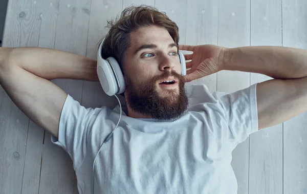 Man luistert naar muziek in witte koptelefoon in de buurt van het raam op de vensterbank rust — Stockfoto