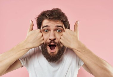 Beyaz tişörtlü neşeli bir adam ellerini pembe arka planda gezdiriyor.