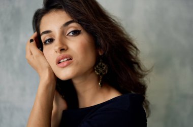 Saçları dağınık güzel bir kadın duvarın yanında poz veriyor.