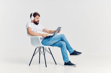 Kulaklıklı dizüstü bilgisayarlı bir sandalyede oturan genç adam. 