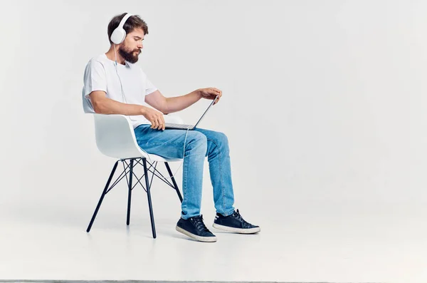Uomo barbuto seduto su una sedia con un computer portatile in cuffie intrattenimento — Foto Stock