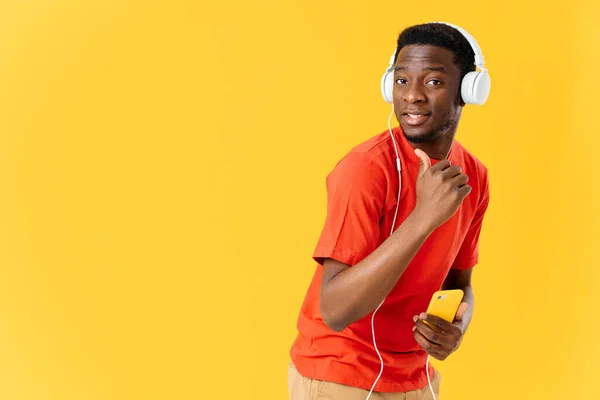 Homem sorridente em fones de ouvido com um telefone em suas mãos em um fundo amarelo — Fotografia de Stock