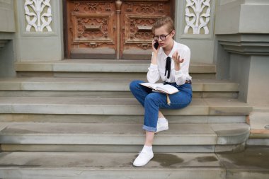 Kısa saçlı, gözlüklü bir kadın elinde bir kitapla şehirde dolanıyor.