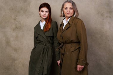 Genç ve yaşlı kadınlar, sonbahar moda stüdyosunun izole edilmiş arka planında yan yana duruyorlar.