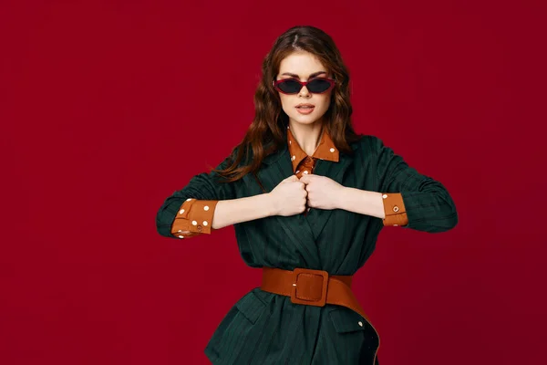 Mujer de moda en traje gesto con las manos gafas de sol de lujo fondo rojo —  Fotos de Stock