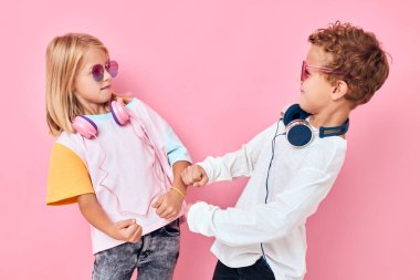 Güneş gözlüklü sevimli çocuklar pembe arkaplanlı arkadaşlarıyla eğleniyor.