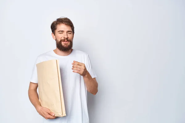 Un hombre con una camiseta blanca con una bolsa de papel en las manos sobre un fondo claro — Foto de Stock