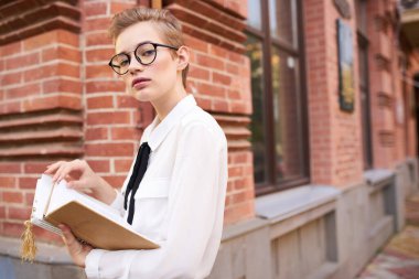 Gözlüklü bir öğrenci elinde bir kitapla şehirde dolaşıyor.