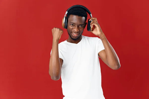 Hombre alegre con auriculares en una camiseta blanca escuchando música entretenimiento fondo rojo — Foto de Stock