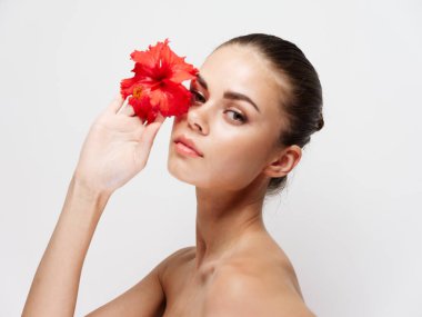 Elinde çiçek olan genç bir kadının portresi açık bir arka planda temiz cilt kozmetolojisi.