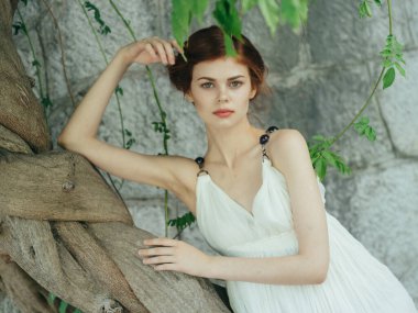 Ağaç tabanlı taş duvarın yanında beyaz elbiseli çekici kadın.