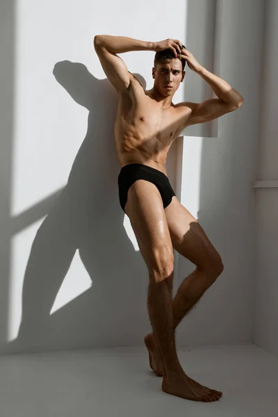 Homem desportivo com um corpo muscular em calcinha preta posando perto da janela — Fotografia de Stock