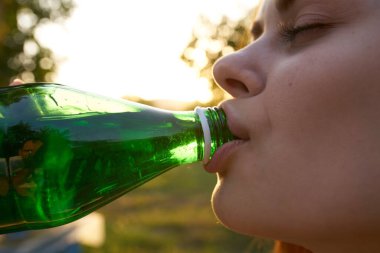 Yeşil bir şişeden su içen kadın doğayı yakından izler.