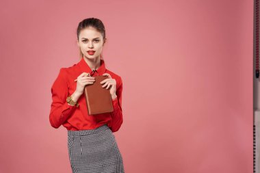 Kırmızı tişörtlü iş kadını. İş yerindeki profesyonellerin elinde not defteri var. Pembe arka plan.