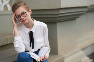 Binanın yakınındaki sokakta elinde kitapla oturan kısa saçlı kadın. 