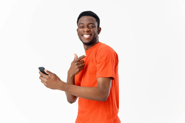 Cara bonito de aparência africana sorri e detém um telefone celular em sua mão — Fotografia de Stock