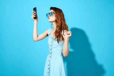 Mavi arka planda telefonu olan mavi elbiseli güzel bir kadın. Yüksek kalite fotoğraf