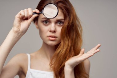 Beyaz tişörtlü, kızıl saçlı kadın. Yüzünde sivilceler.