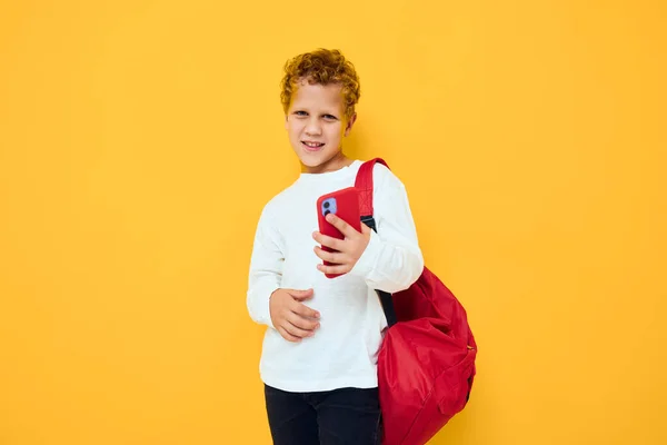 Garotinho sorridente com uma mochila vermelha chama no telefone fundo amarelo — Fotografia de Stock