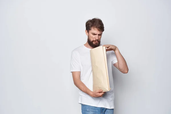 Homem barbudo em uma camiseta branca com um pacote em suas mãos emoções mockup — Fotografia de Stock