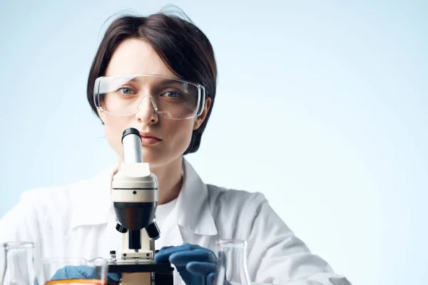 Assistente di laboratorio seduto al tavolo microscopio ricerca biotecnologia sfondo chiaro — Foto Stock