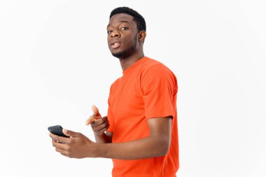 Cep telefonu ve açık arkaplanda turuncu tişörtlü Afro-Amerikan.