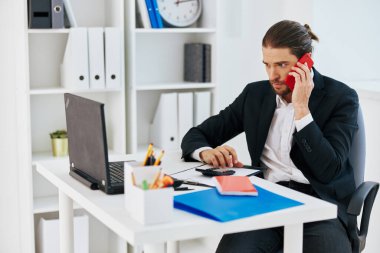 Yönetici ofisi, elinde telefon teknolojisiyle evrak işleriyle uğraşıyor.
