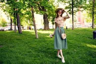 Neşeli kadın yaz tatilinde bir içkiyle parkta yürüyor.