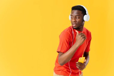 Afrika kökenli, kulaklıklı müzik dinleyen sarı arka planlı bir adam.